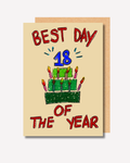 A greeting card with a hand-drawn style illustration of a birthday cake and candles, with the text 'BEST DAY OF THE YEAR' and a large blue '18' on the front, shown with a kraft envelope behind it.